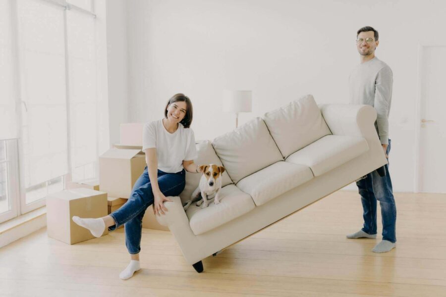 Man lifting a couch with a woman and a dog on it