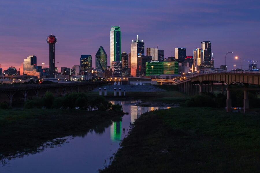 Night view of the downtown Dallas skyline with illuminated skyscrapers reflecting over the Trinity River