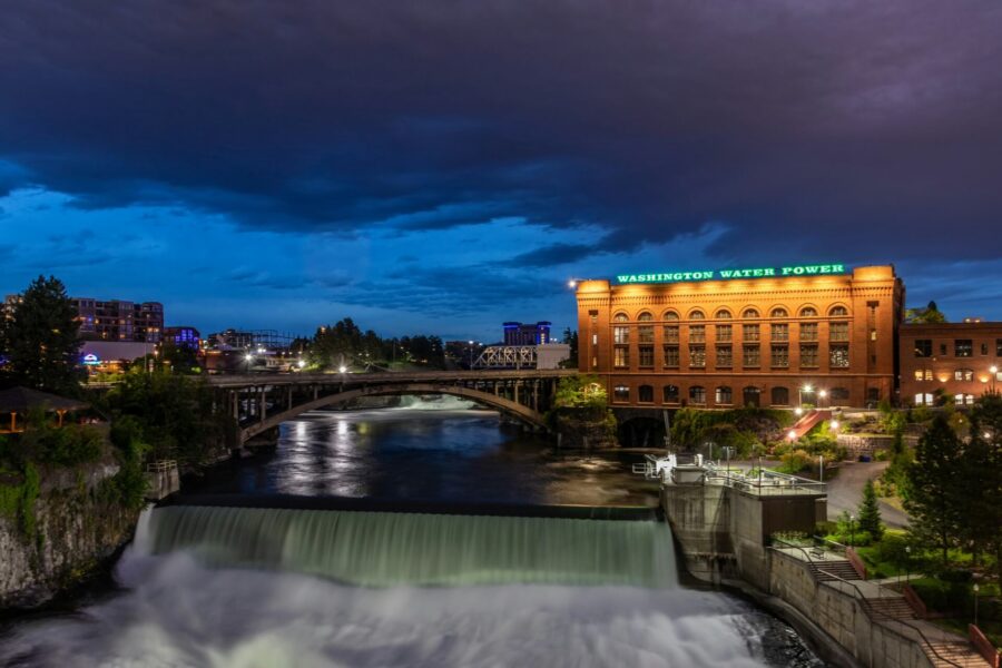 Illuminated water fountain spraying blue-lit streams at night in front of city buildings in Spokane, Washington.